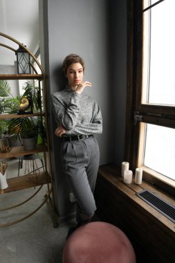 Stüdyoda poz veren genç ve güzel bir kadın. Pencere kenarında süveter giyiyor.