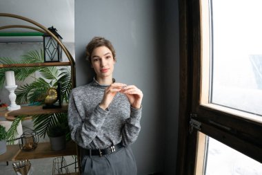 Stüdyoda poz veren genç ve güzel bir kadın. Pencere kenarında süveter giyiyor.