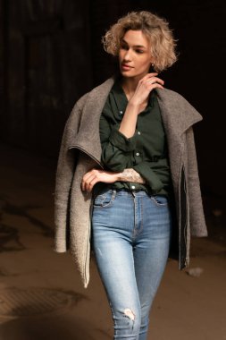 Dışarıdan ceketli ve kotlu güzel bir kadın poz veriyor.