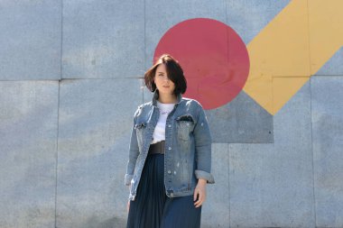 Genç ve güzel bir kadın dışarıda kot ceketle poz veriyor.