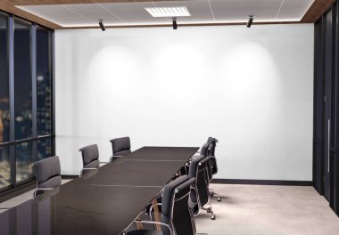 Blank white wall Mockup in dark modern office with windows and bright spotlights. Empty company meeting room 3D rendering