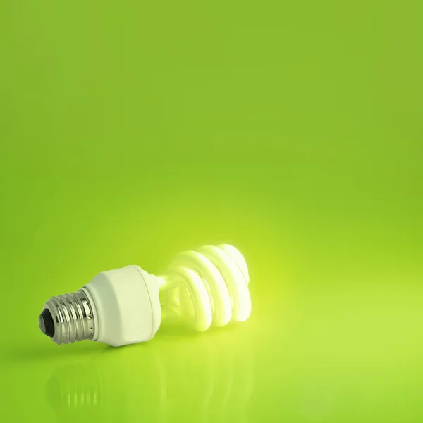 A vibrant presentation of a modern energy-saving light bulb lit on a lush green background. Plenty of copy-space, ideal for ecology, energy concepts - perfect for slides and presentations — Stock Photo, Image