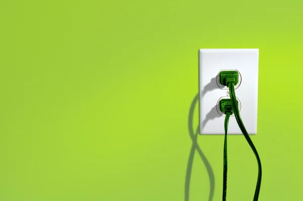 Zelená napájecí šňůry do zásuvky na zelené barevné zdi - zelené energetické koncepce Stock Snímky