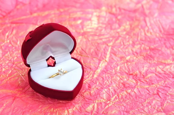 Κόκκινο βελούδο σχήμα καρδιάς δώρο κουτί με χρυσό δαχτυλίδι σε φόντο ένα χαρτί περιτυλίγματος — Φωτογραφία Αρχείου