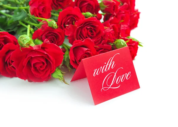 Rosas vermelhas são com o cartão de saudação em um fundo branco — Fotografia de Stock