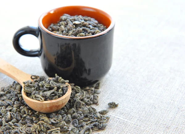 Trockener grüner Tee in einem Löffel und einer Tasse auf einem Sacktuch — Stockfoto