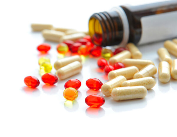 Pills pouring out of the brown bottle on a white background