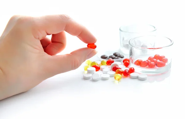 Red capsule in a hand on a white background with glass and pills — Stock Photo, Image