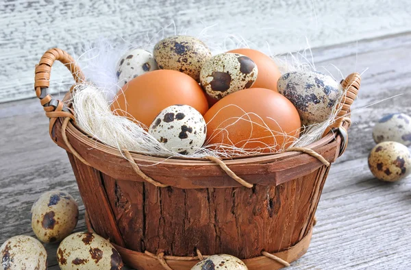 Verschillende soorten eieren in een mand op een oude houten achtergrond — Stockfoto