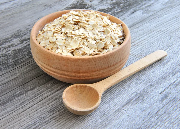 Fiocchi d'avena in ciotola e cucchiaio di legno su sfondo vecchio di legno — Foto Stock