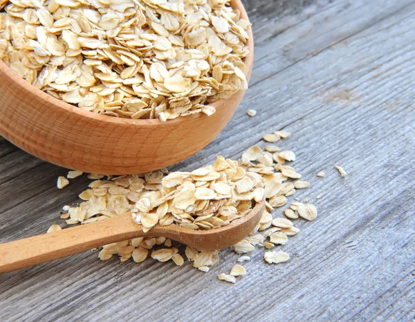 Oat flakes in bowl and wooden spoon on old wooden background — Stock Photo, Image