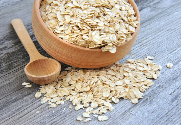 Oat flakes in bowl and wooden spoon on old wooden background — Stock Photo, Image