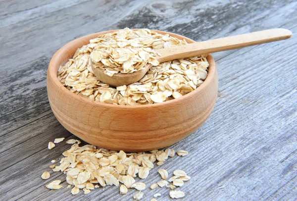 Fiocchi d'avena in ciotola e cucchiaio di legno su sfondo vecchio di legno — Foto Stock