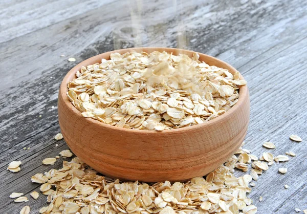 Oat flakes spilling in a wooden bowl on old wooden background — Stock Photo, Image