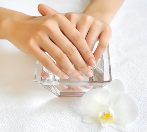 Mãos de mulher em tigela de vidro com água em uma toalha branca — Fotografia de Stock