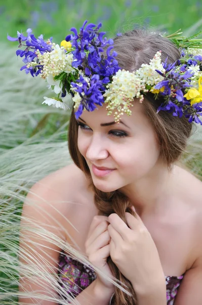 Belle jeune femme avec une couronne de fleurs dans l'herbe de plumes-herbe à l'extérieur — Photo