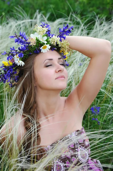 Beautiful young woman with flower wreath in the grass of feather-grass outdoors — Stock Photo, Image