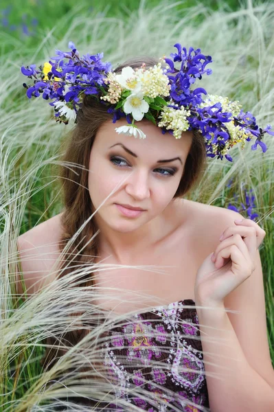 Schöne junge Frau mit Blumenkranz im Gras des Federgrases im Freien — Stockfoto