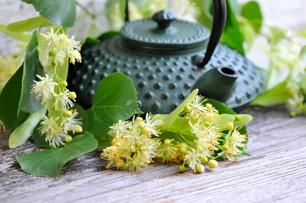 Teapot with linden tea and flowers on old wooden background — Stock Photo, Image