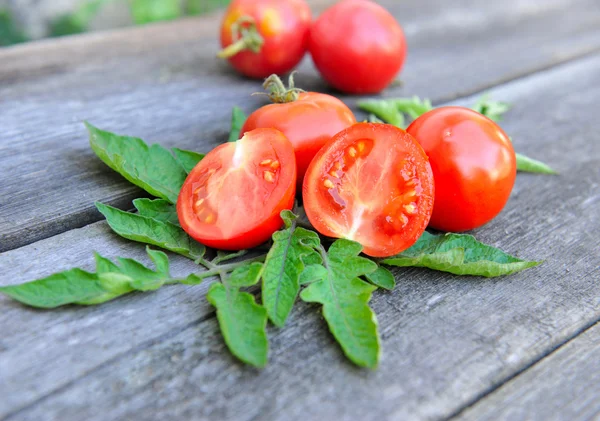 Los tomates están con hojas en una vieja mesa de madera —  Fotos de Stock