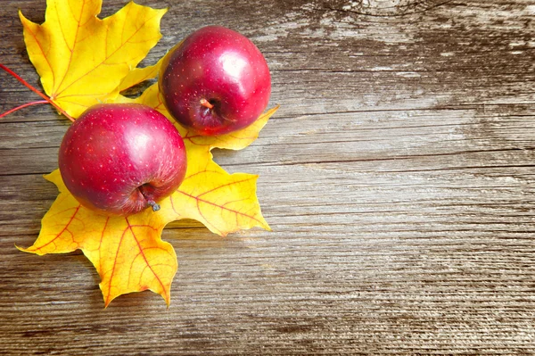 Red apples are with autumn leaves over old wooden background. With copy space — Stock Photo, Image