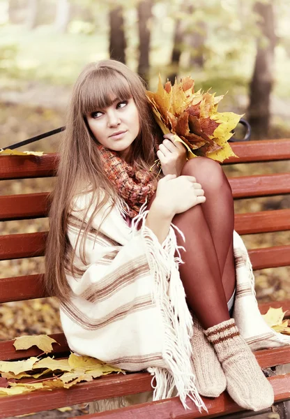 Krásná mladá žena sedí na lavičce s listím — Stock fotografie