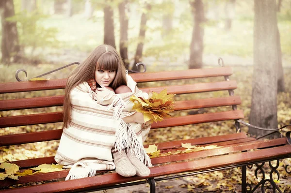 Schöne junge Frau sitzt auf einer Bank in einem herbstlichen Park — Stockfoto
