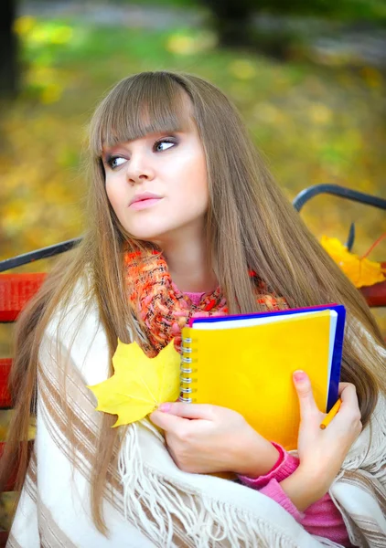 Schöne junge Mädchen ist mit einem Notizbuch in einem Park — Stockfoto