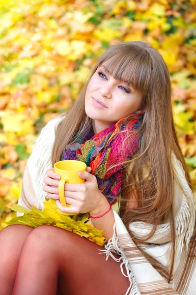 Junge schöne Frau, die die Tasse Tee in Händen hält auf einem Hintergrund Herbstblätter — Stockfoto