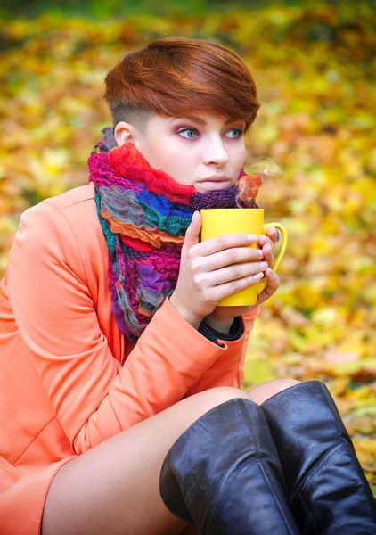 Junge schöne Frau, die die Tasse Tee in Händen hält auf einem Hintergrund Herbstblätter — Stockfoto