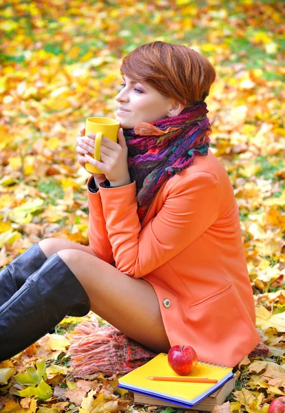 Joven mujer hermosa que sostiene la taza de té en las manos sobre un fondo hojas de otoño — Foto de Stock