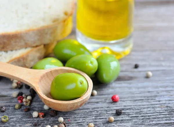 Groene olijven in een houten lepel met olie en paprika's op een houten achtergrond kleur — Stockfoto