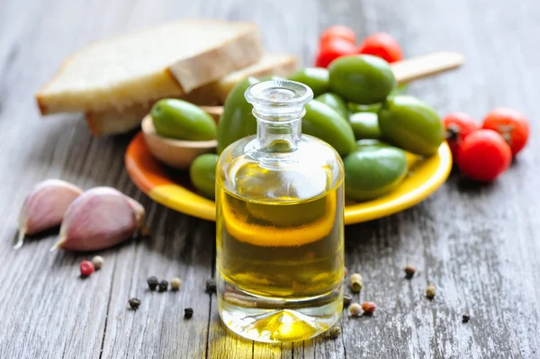 Een fles van olie, olijven en kruiden op een houten achtergrond — Stockfoto