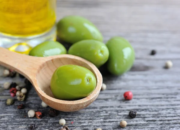 Olives vertes dans une cuillère en bois avec de l'huile et des poivrons de couleur sur un fond en bois — Photo