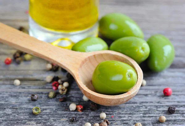 Groene olijven in een houten lepel met olie en paprika's op een houten achtergrond kleur — Stockfoto