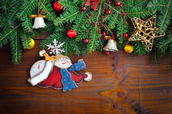 Branches of fir with snowman and Christmas decorations on wooden background — Stock Photo, Image