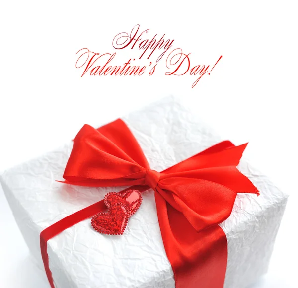 Gift with red satin bow and two hearts on white — Stock Photo, Image