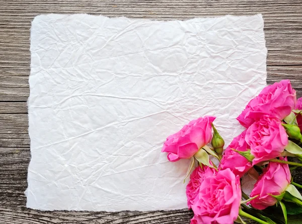 Tarjeta blanca y rosas rosadas sobre fondo de madera —  Fotos de Stock