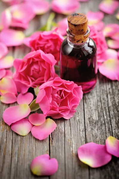 Aceite esencial con pétalos de rosa sobre fondo de madera —  Fotos de Stock