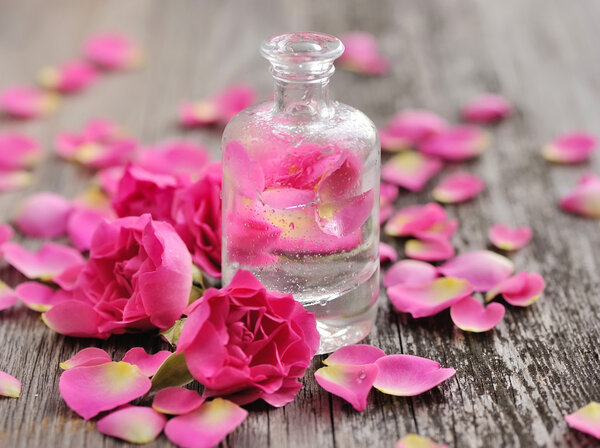 Essential oil with rose petals on wooden background