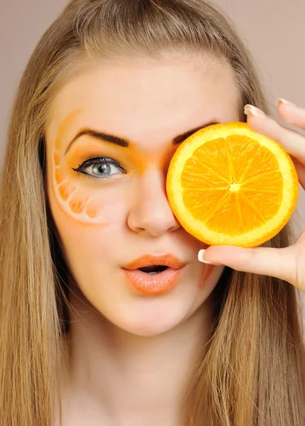 Jonge mooie vrouw met creatieve oranje make-up met oranje in haar hand — Stockfoto