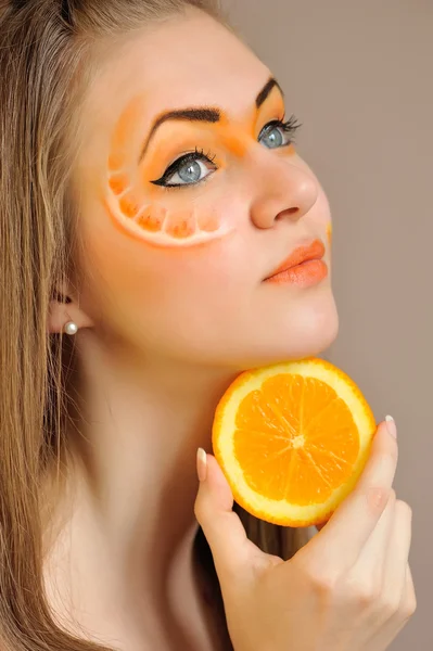 Jonge mooie vrouw met creatieve oranje make-up met oranje in haar hand — Stockfoto