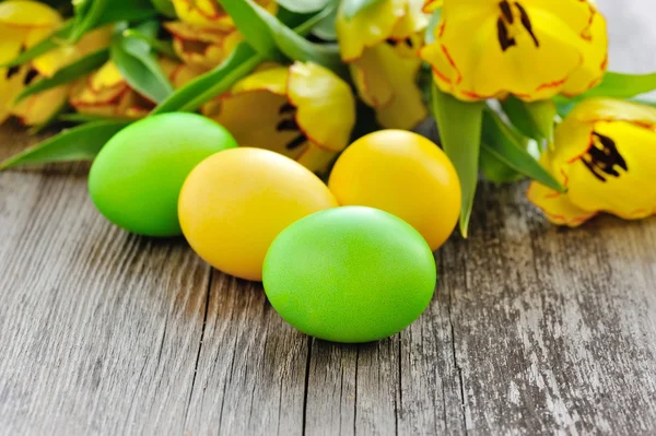 Ovos de Páscoa com tulipas na velha mesa de madeira — Fotografia de Stock