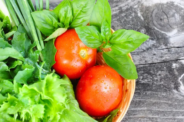 Fresh vegetables and greenery are in a basket on a old wooden background — Stock Photo, Image