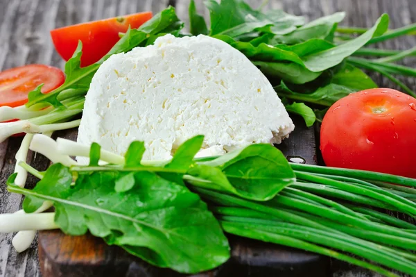 Cheese with tomatoes and arugula and onion on a wooden board — Stock Photo, Image