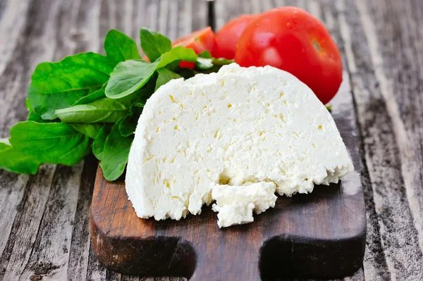 Queijo com tomate e arugula em uma tábua de madeira — Fotografia de Stock