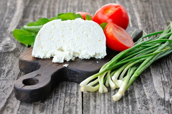 Cheese with tomatoes and arugula and onion on a wooden board — Stock Photo, Image