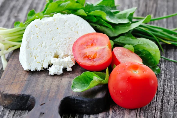 Сыр с помидорами и рукколой и луком на деревянной доске — стоковое фото