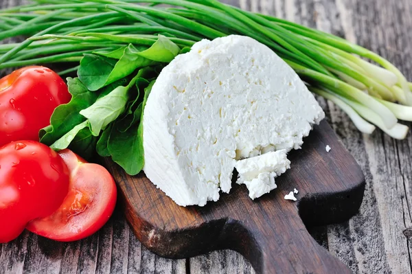 Cheese with tomatoes and arugula and onion on a wooden board — Stock Photo, Image