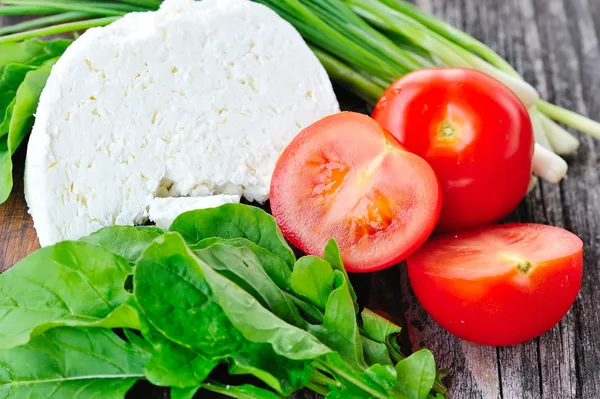 Cheese with tomatoes and arugula and onion on a wooden board — Stock Photo, Image